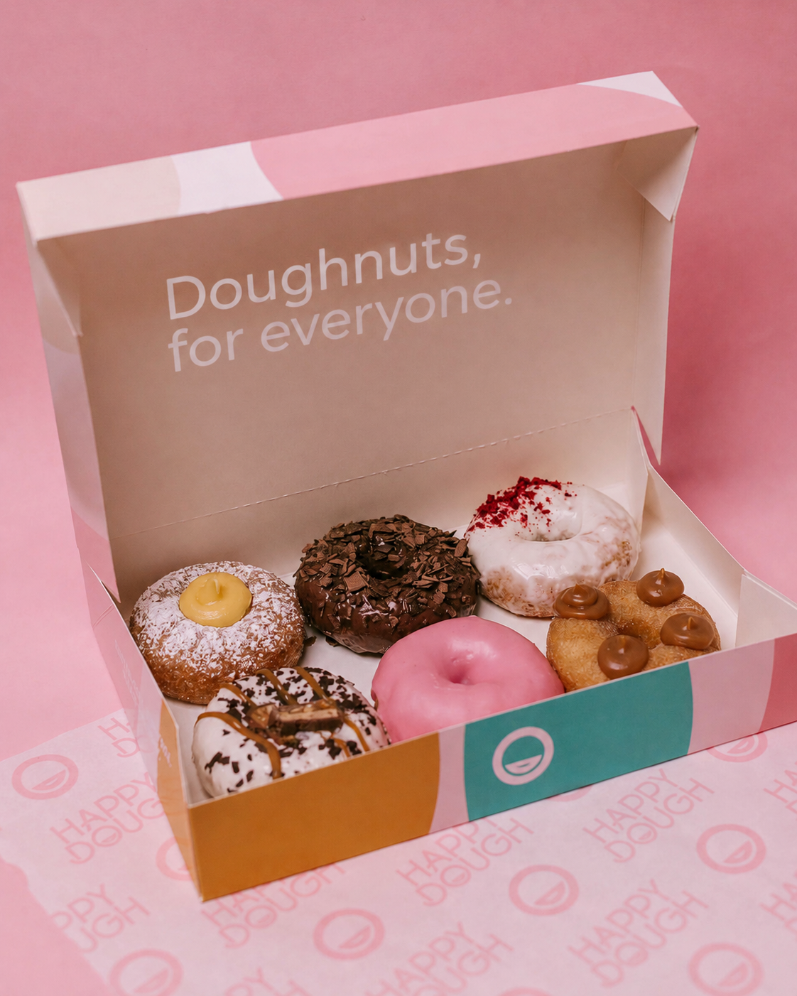 An open box of six Happy Dough gluten-free doughnuts on a pink background