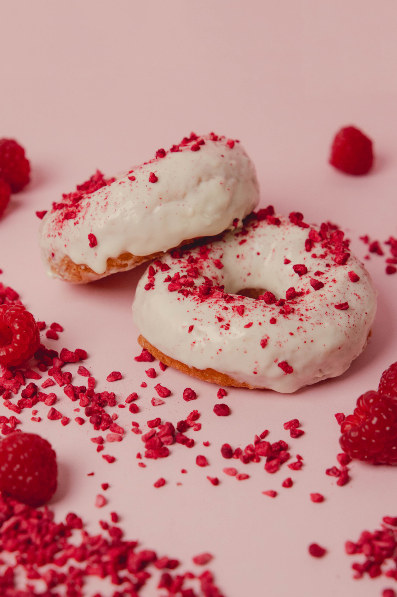 Two gluten-free doughnuts glazed in white chocolate and scattered with freeze-dried raspberry